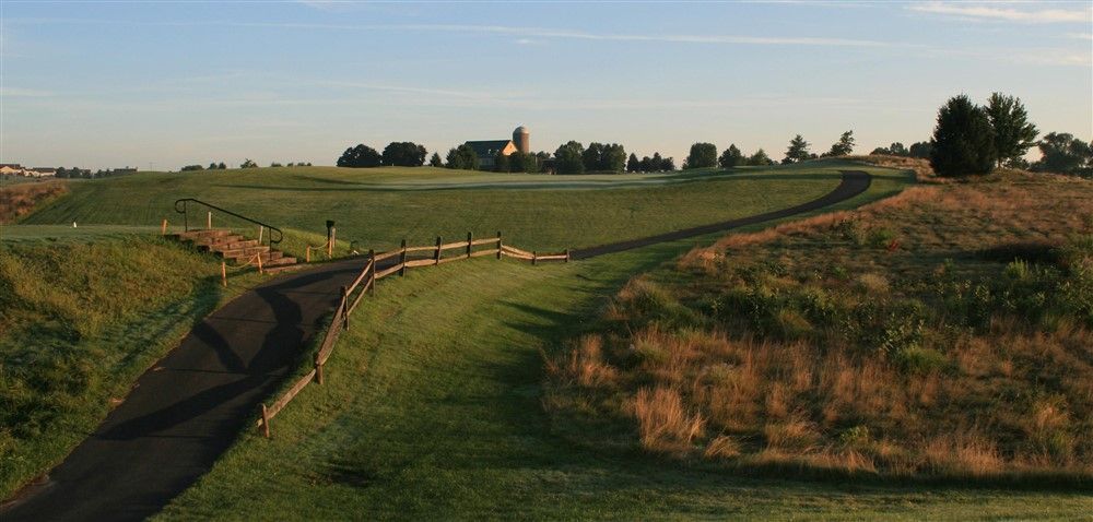 A golf course scene with a paved path winding toward the green and a building on the horizon.
