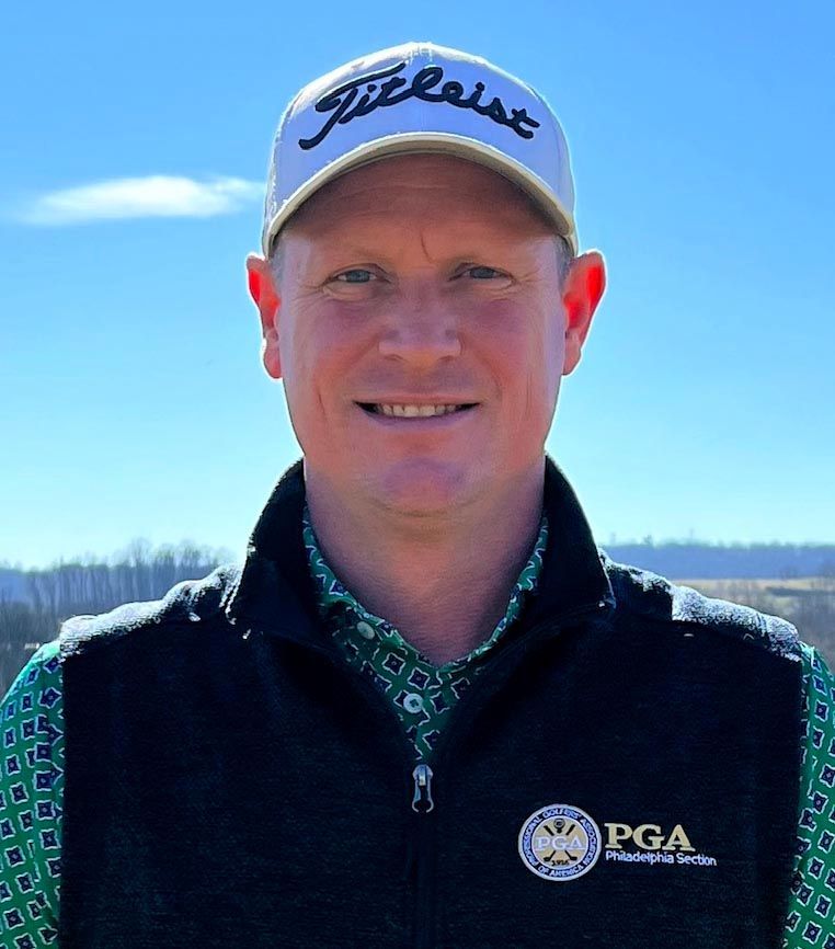 Man wearing a Titleist cap and vest, smiles at the camera; blue sky background.
