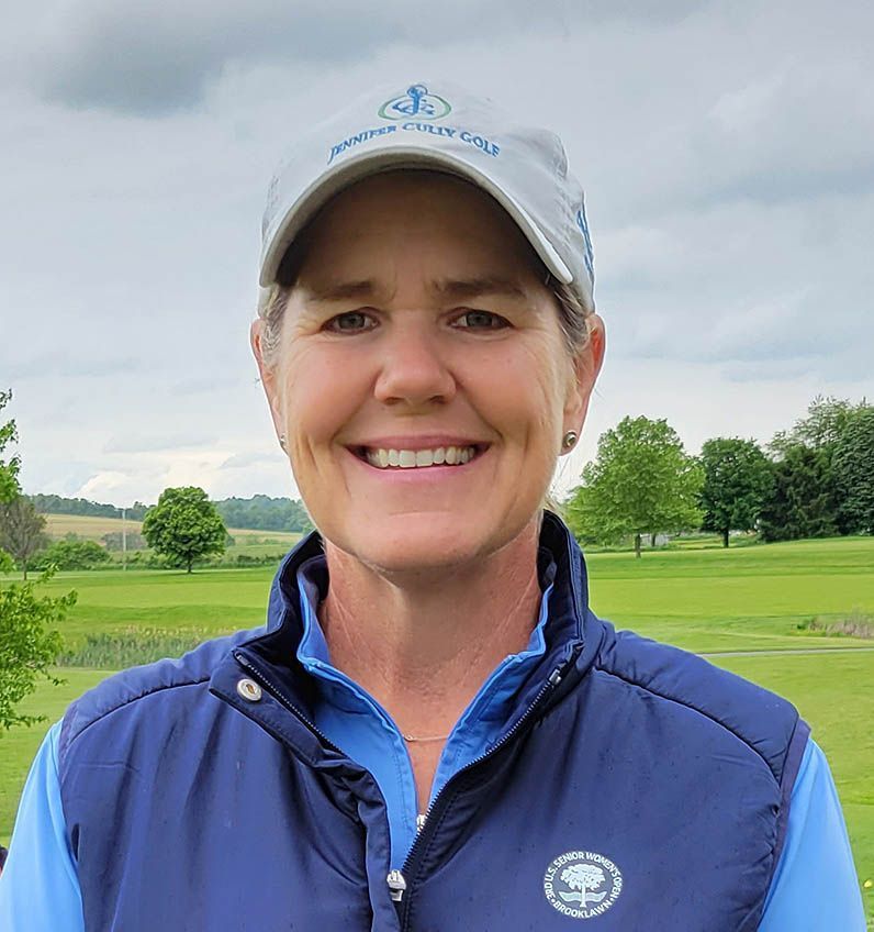 Woman wearing a golf cap and vest smiles outdoors on a golf course.