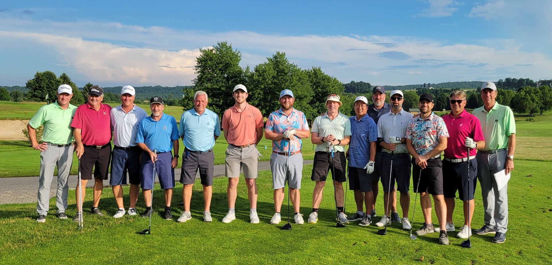 A group of men in golf attire pose on a green course under a blue sky.