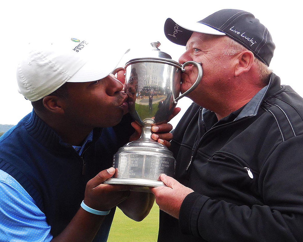 A man kissing another man on the cheek while holding a trophy