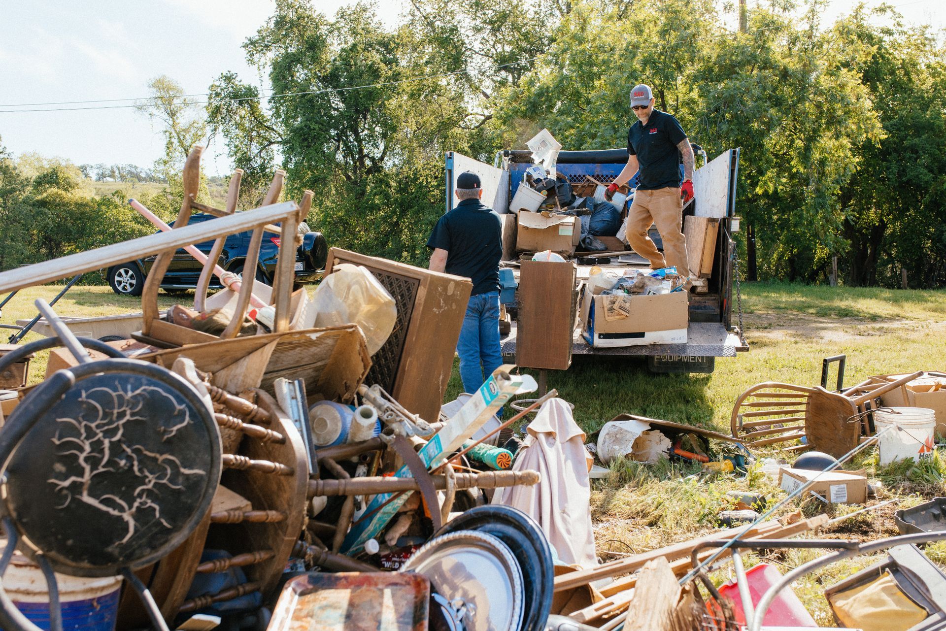 Two men are loading a truck with junk in a field.