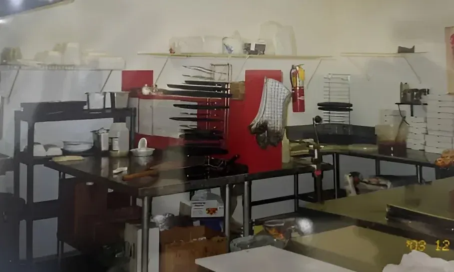 E-Z Riders Pizza kitchen from the early days with stainless steel counters, red accents, and shelves holding supplies.