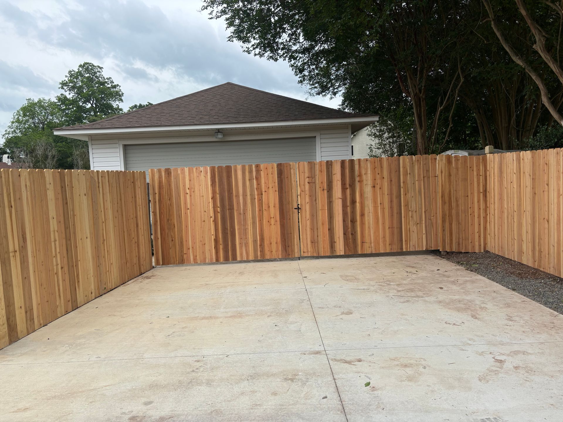 Concrete driveway enclosed by a wooden privacy fence with a house and tree in the background
