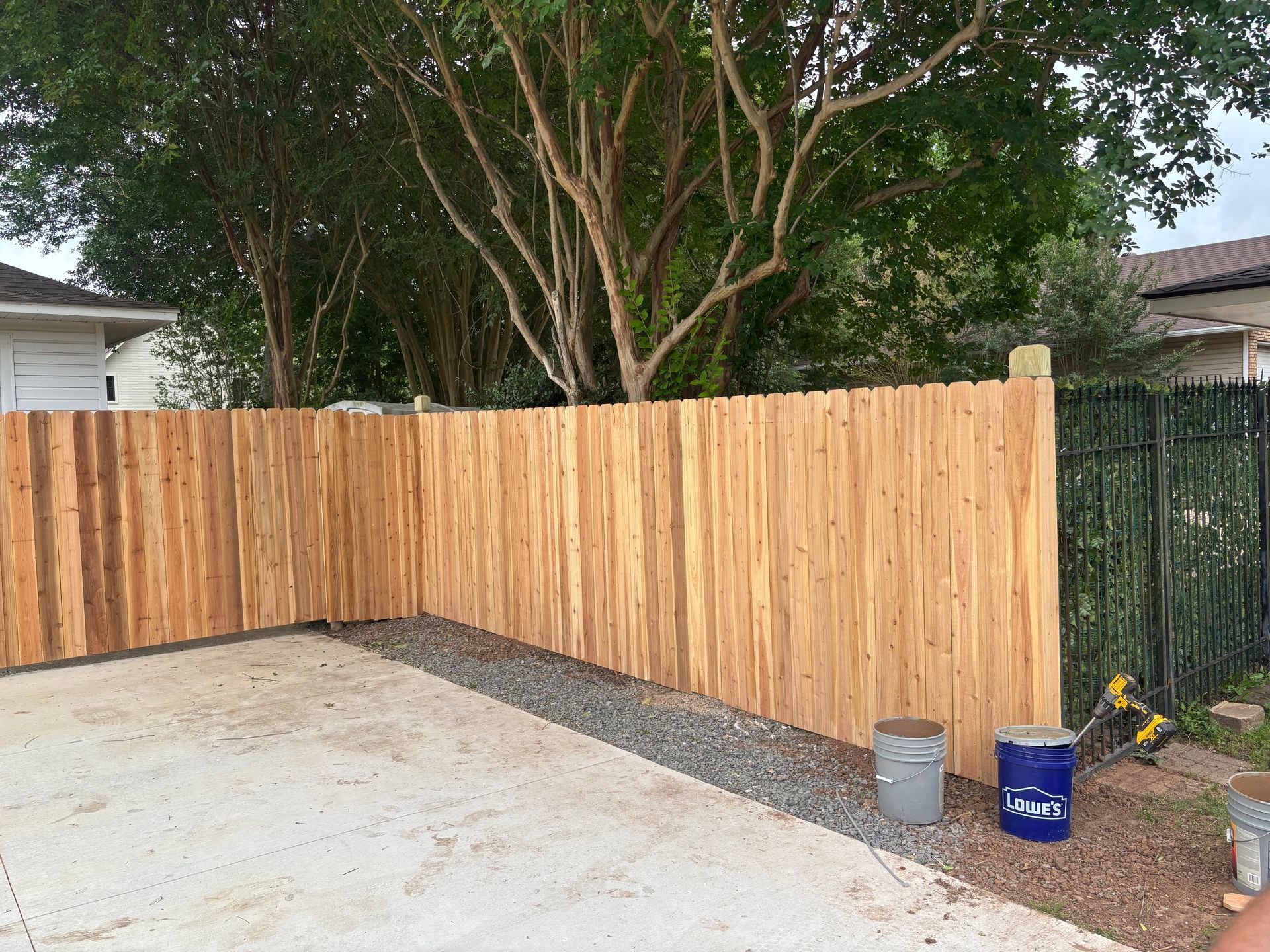 New wooden fence enclosing a concrete driveway, with buckets and garden tools nearby