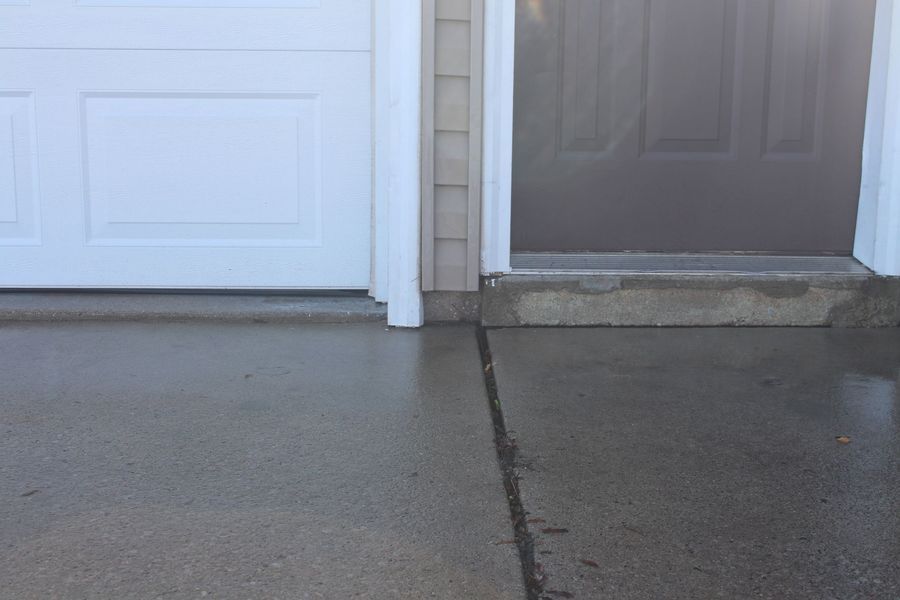 A concrete walkway next to a garage door and a doorway.