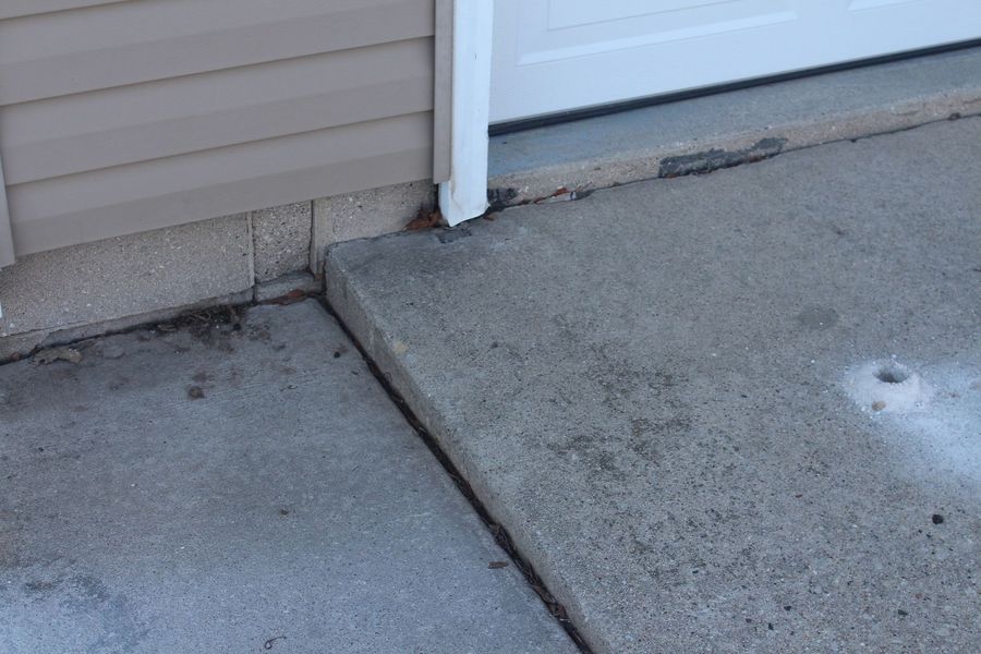 A concrete sidewalk next to a garage door and a house.