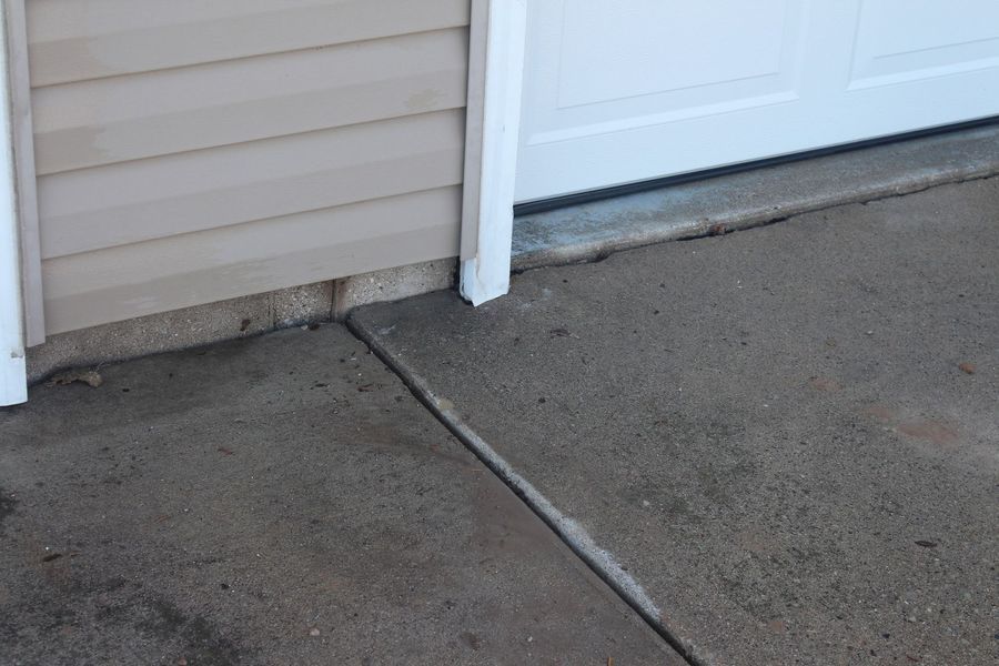 A concrete sidewalk next to a garage door and a house.