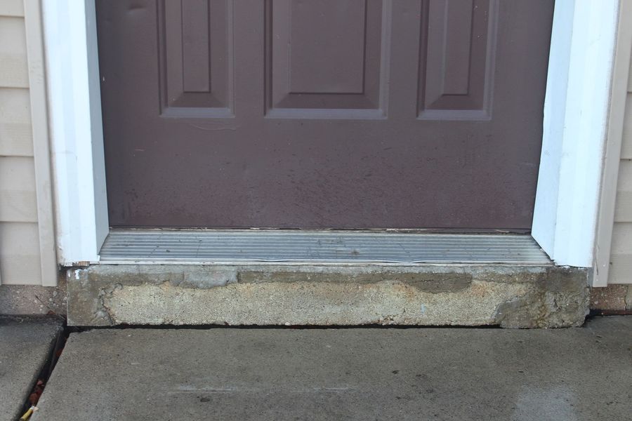 A brown door with a white trim is sitting on a concrete porch.