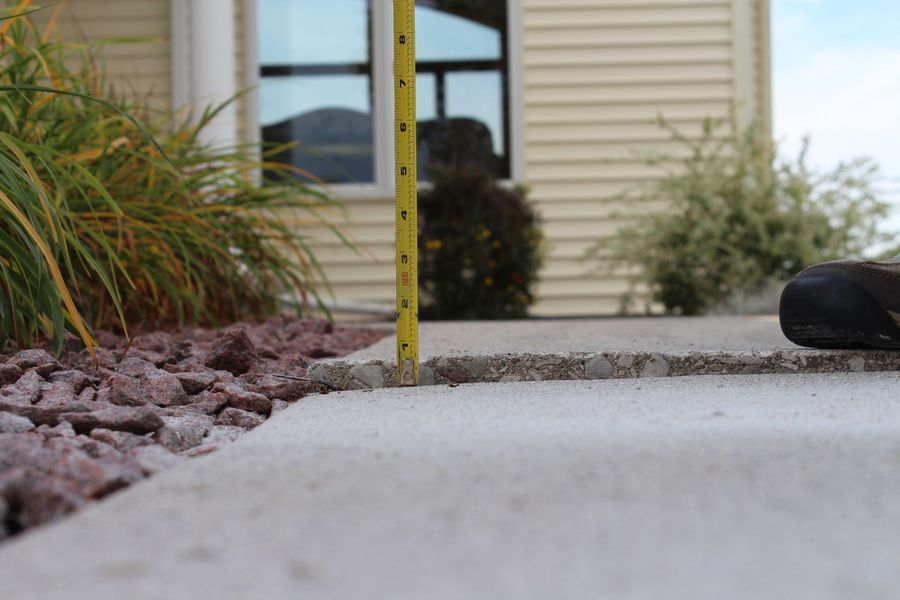 A person is measuring a sidewalk with a tape measure in front of a house.