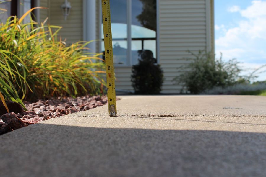 A person is measuring the width of a driveway with a tape measure.
