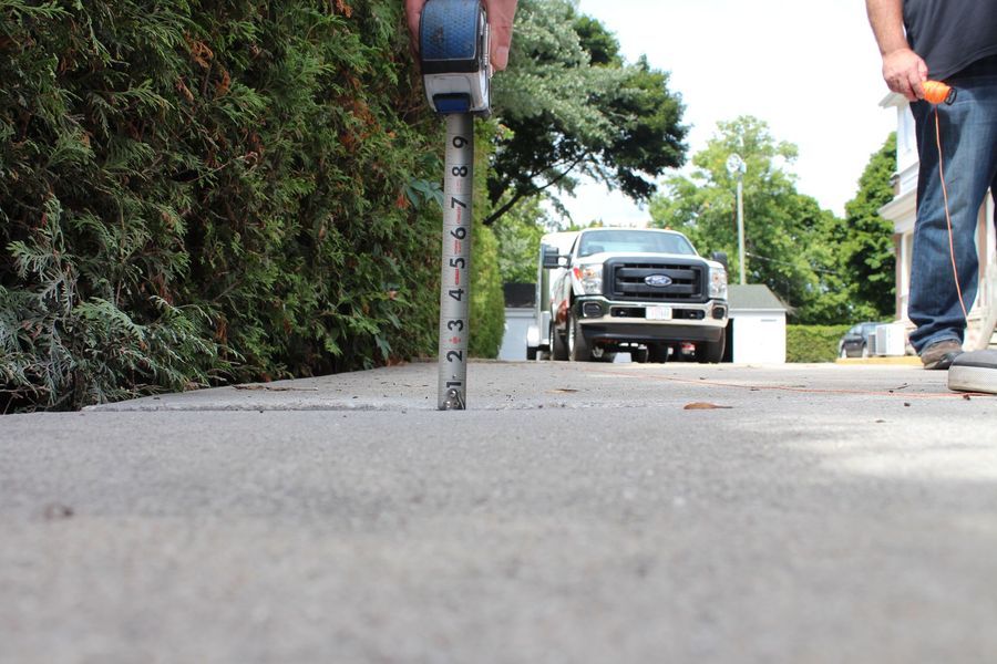 A man is measuring the height of a driveway with a tape measure