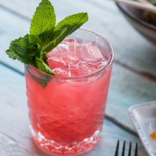 A glass of pink liquid with ice and mint on top