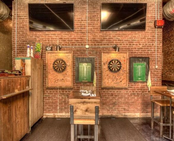 A room with a brick wall and three dart boards on the wall.