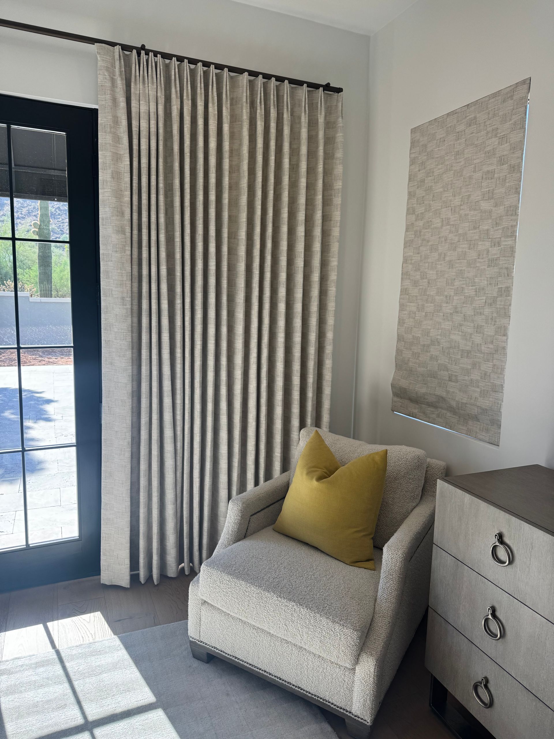 A patterned armchair with a yellow pillow sits beside a floor-to-ceiling curtain and a matching wall shade.