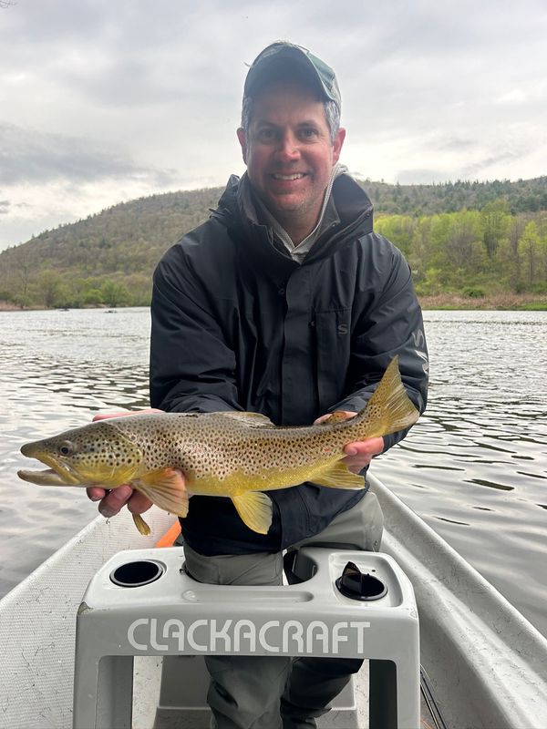 Man in a boat holding a brown trout on a lake with hills in the background