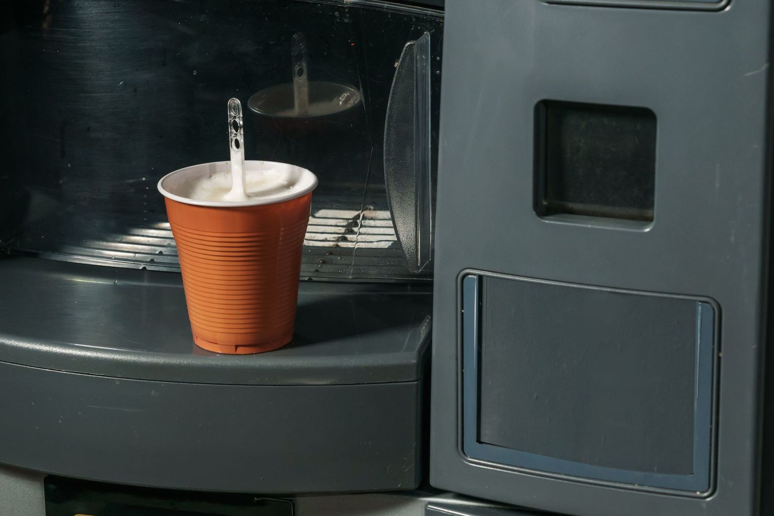 Orange cup with a spoon inside sitting in a coffee machine compartment