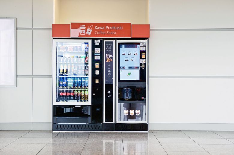 Red vending machine with drinks and a touchscreen on a tiled indoor wall