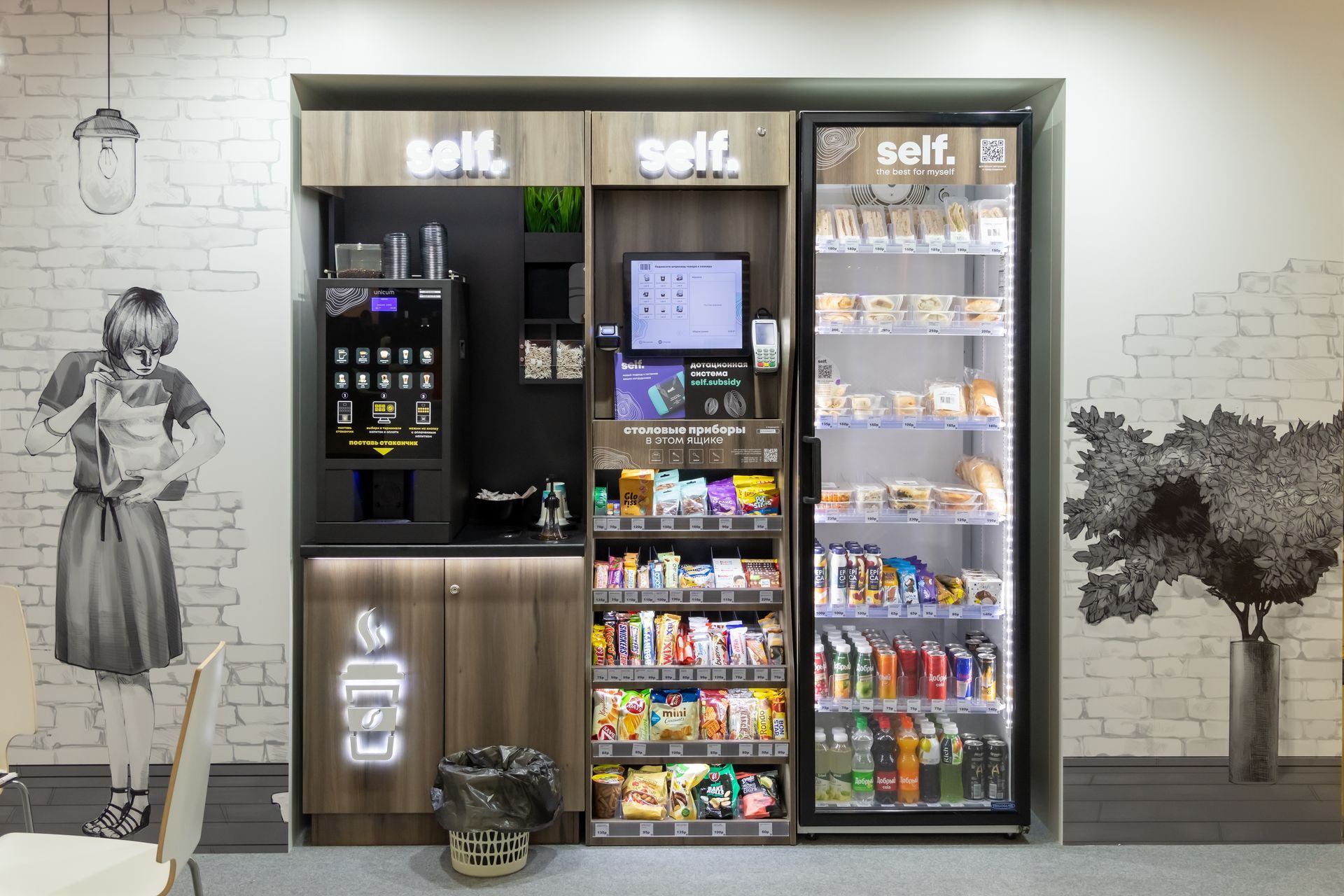 Modern self-service kiosk and snack display against a white brick wall with mural art
