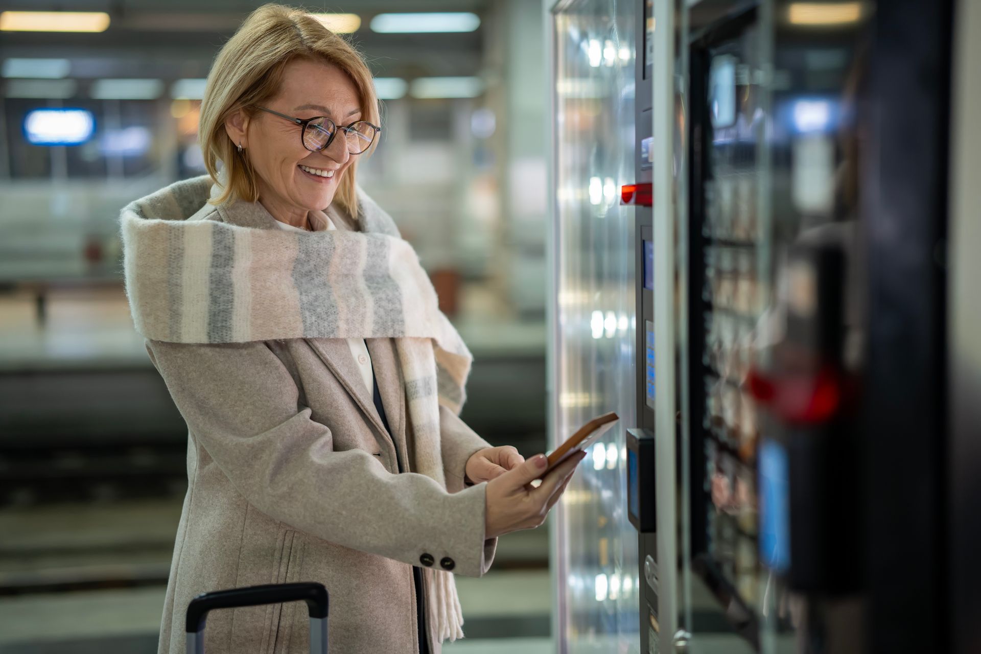 Traveler tapping a ticket machine at a train station, wearing a coat and scarf, with luggage nearby