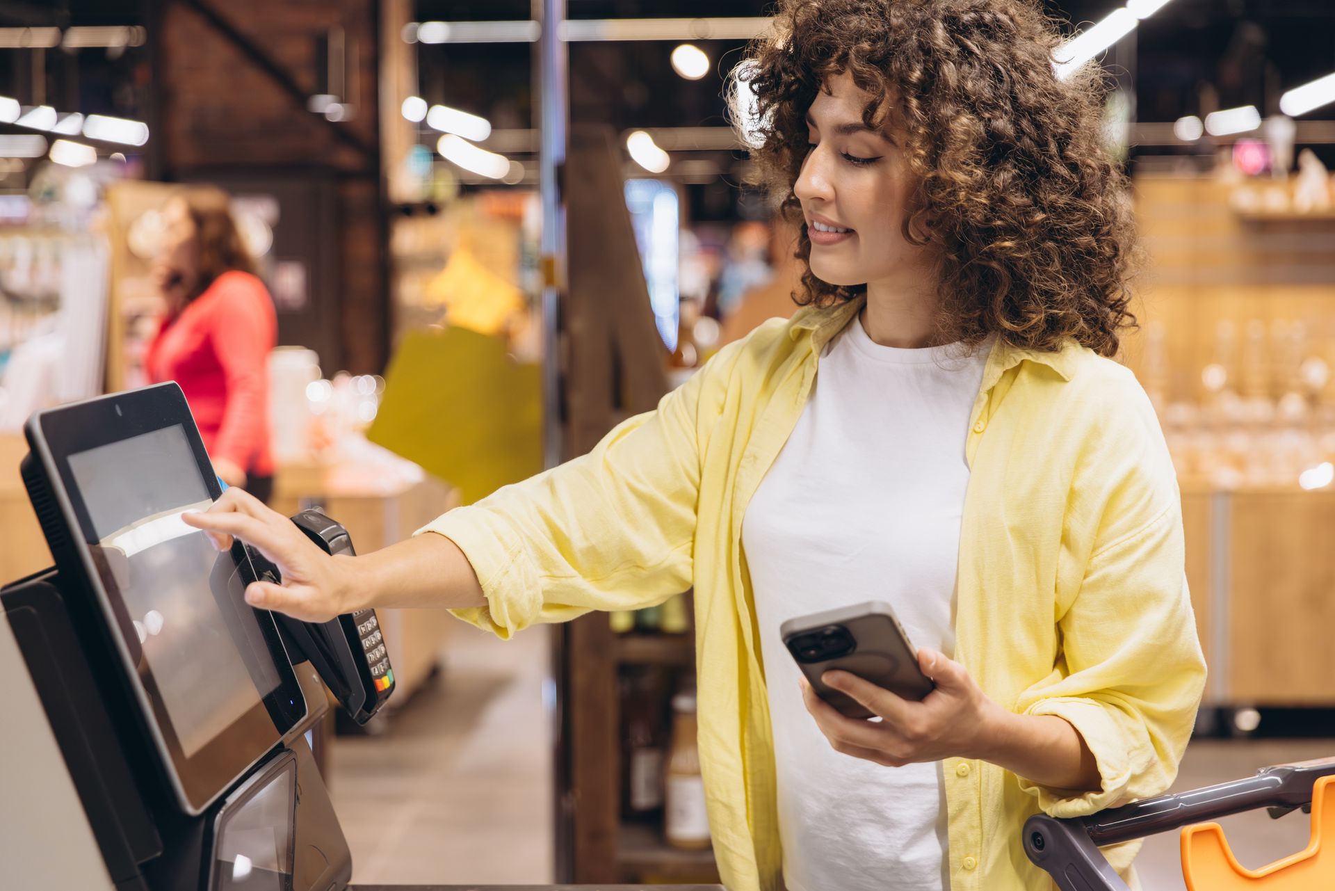Woman using a touchscreen kiosk while holding a phone in a store