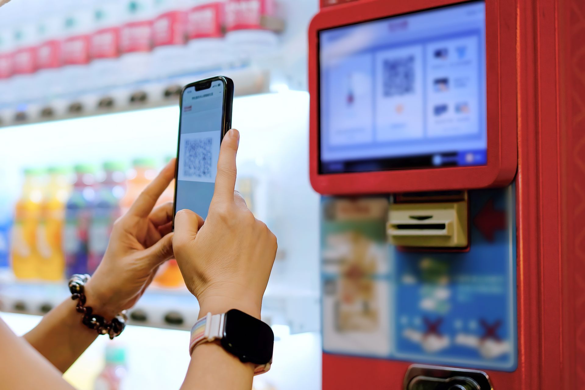 Person using a smartphone to scan a red kiosk in a store aisle