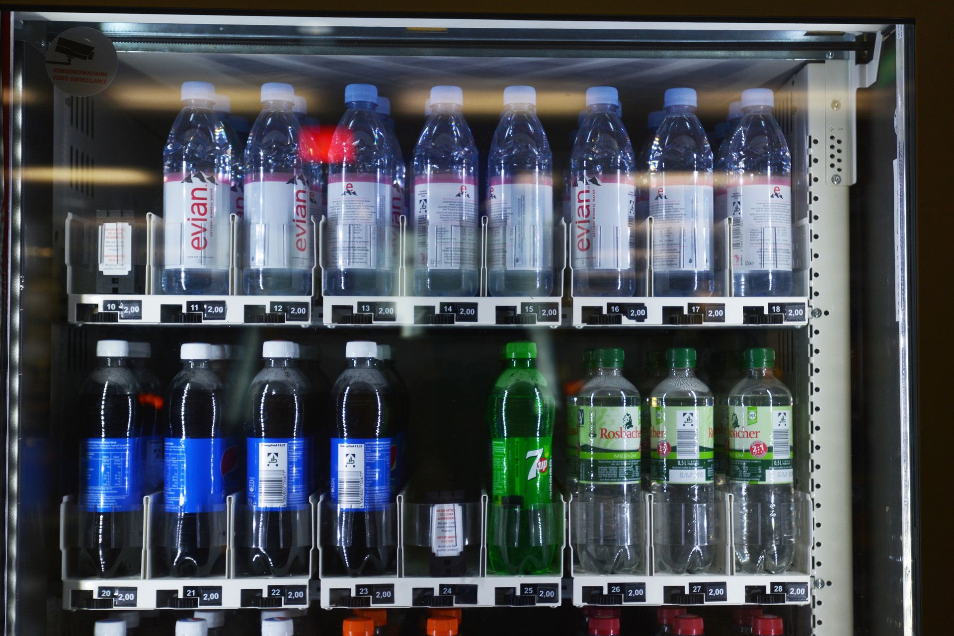 Refrigerated display case with assorted bottled drinks, including water and soda, on two shelves.