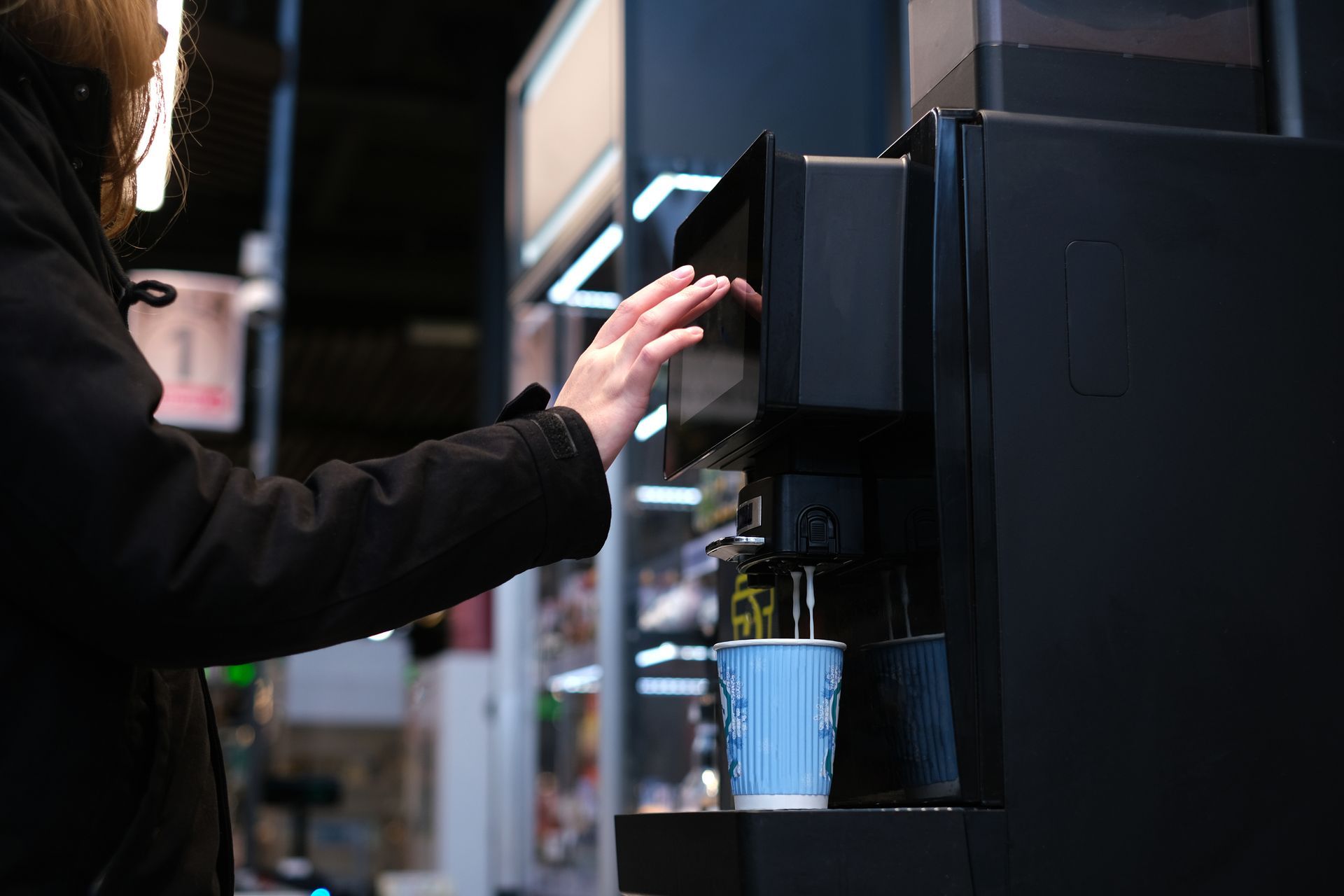 Person using a coffee machine to fill a blue cup in a café setting