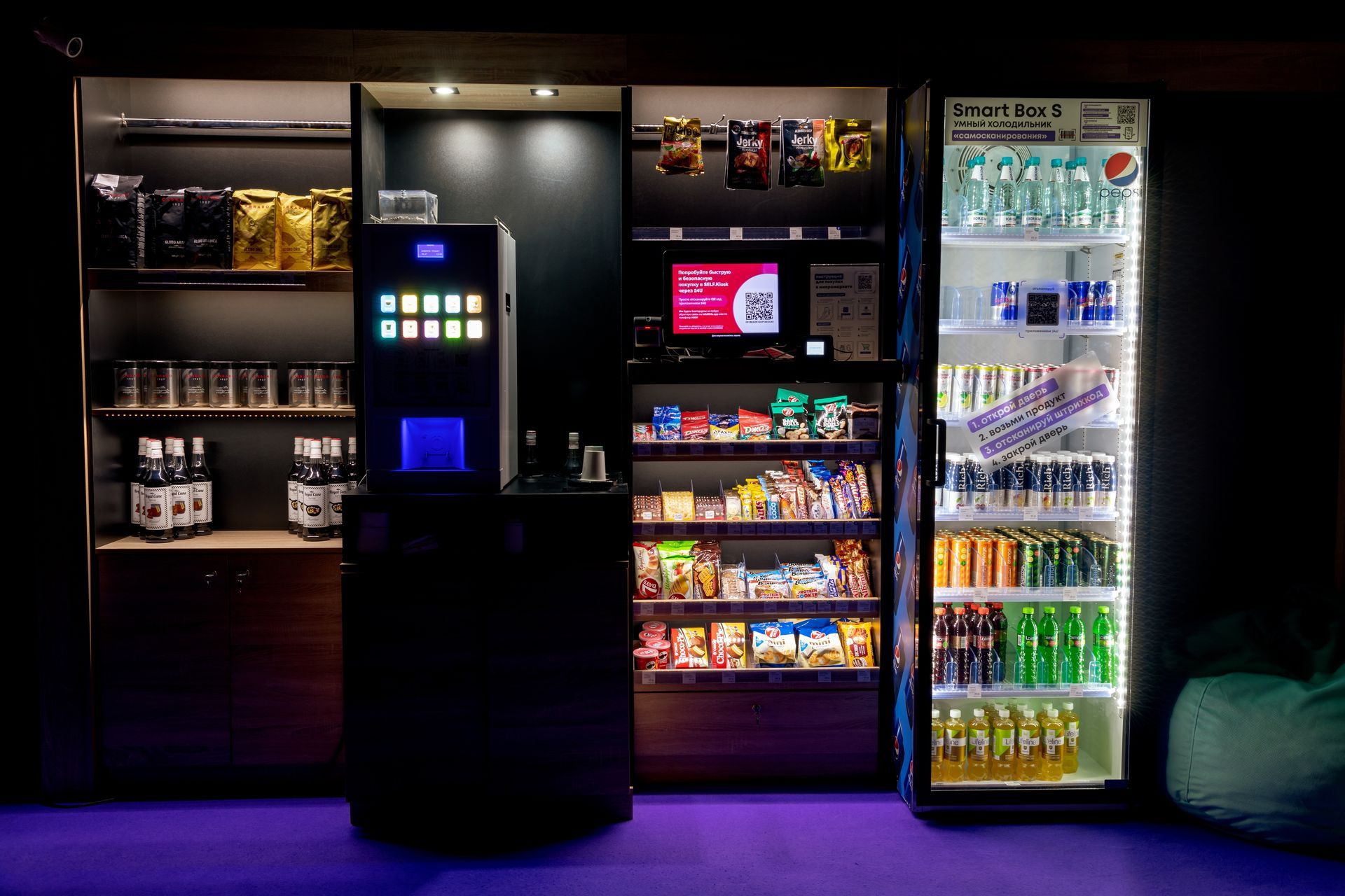 Illuminated snack and drink vending machines in a dim room with a central payment kiosk