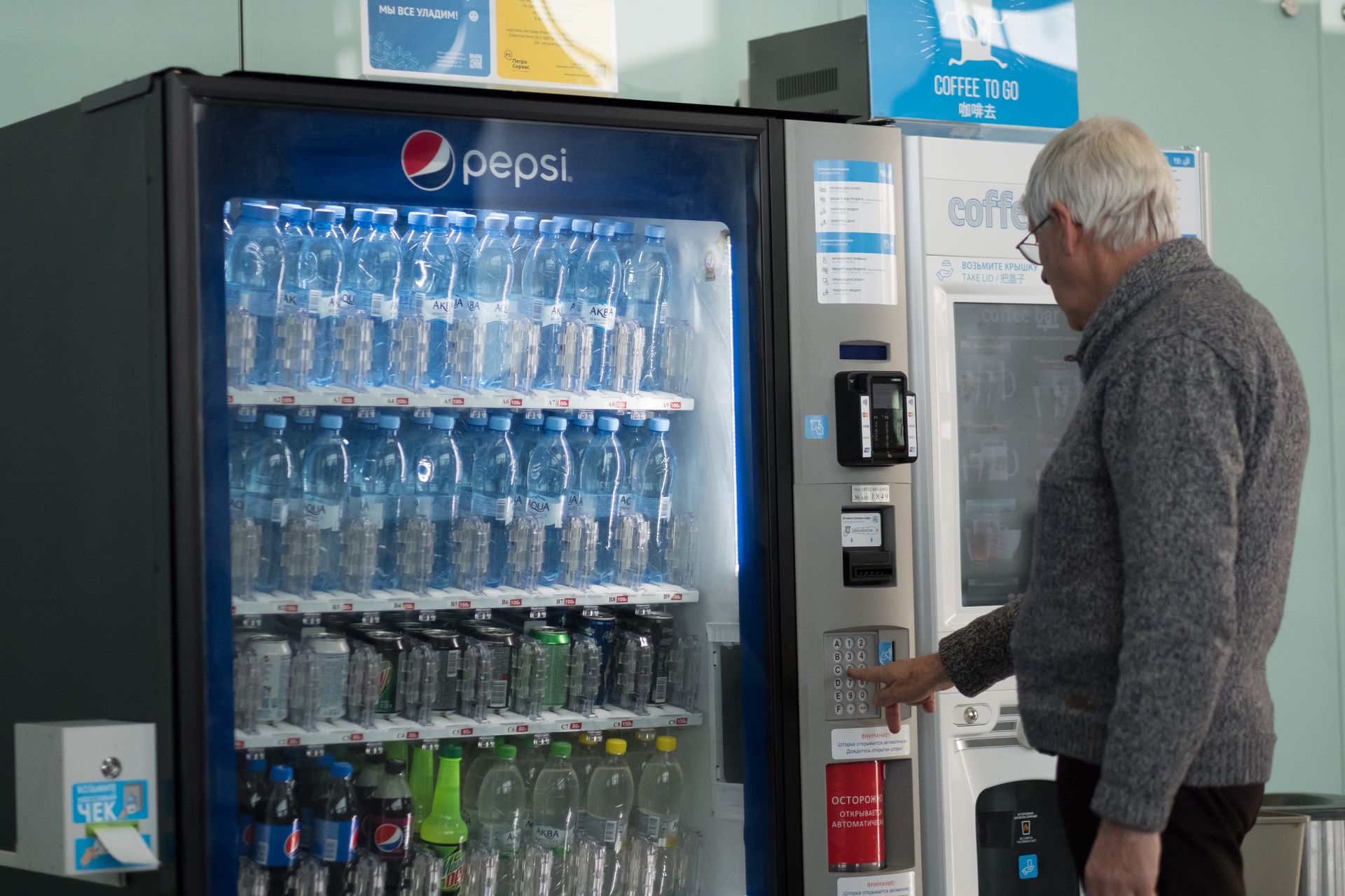 Man selecting a drink from a Pepsi vending machine beside a drink cooler in a store