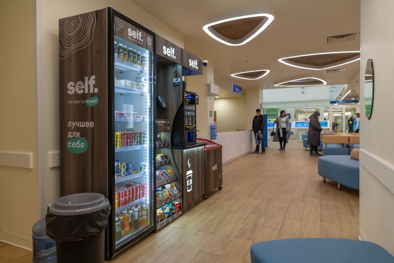 Hospital waiting area with self-checkout kiosks, vending machines, and blue seating