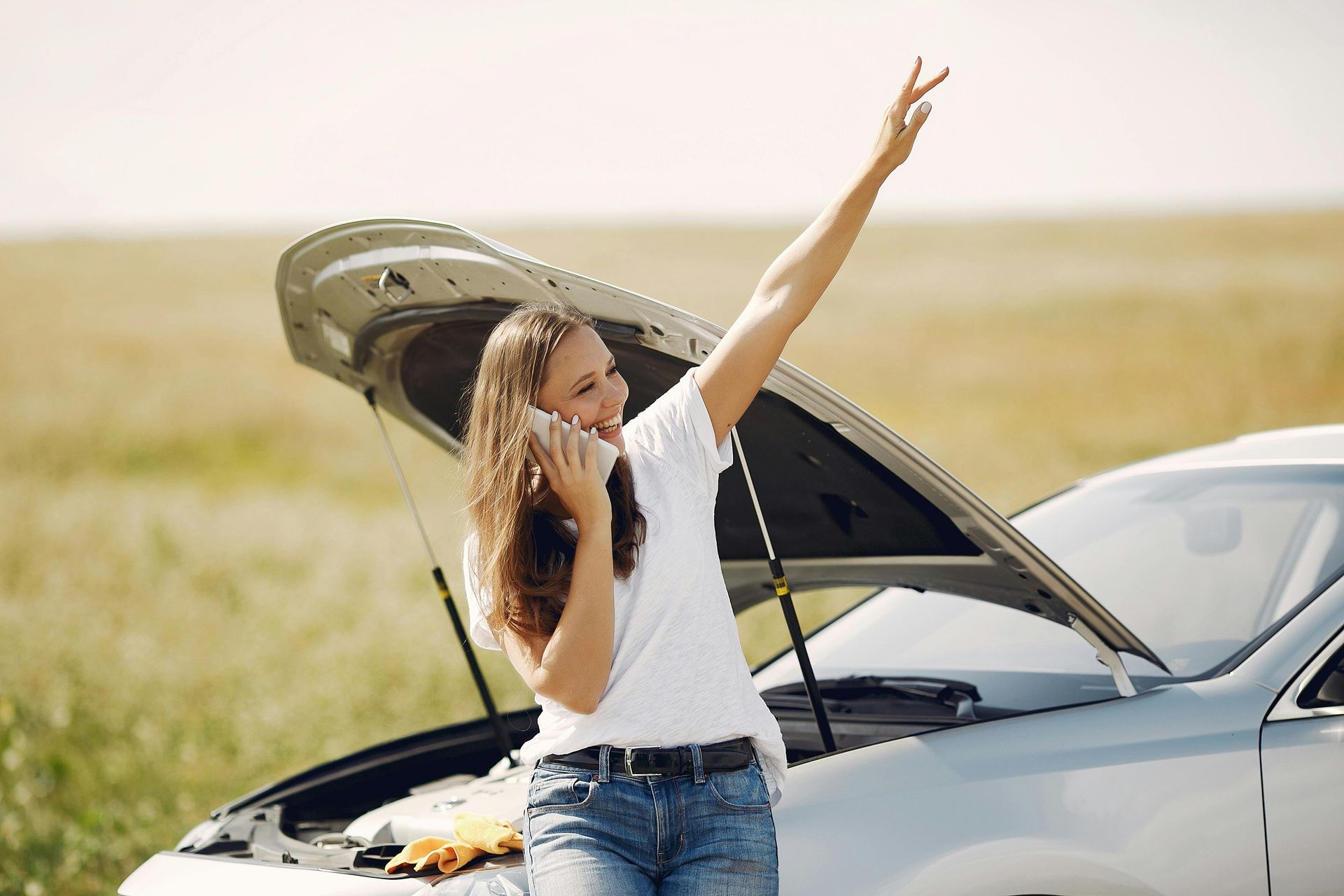 A woman is talking on a cell phone next to a broken down car. Jado Mobile Auto Repair
