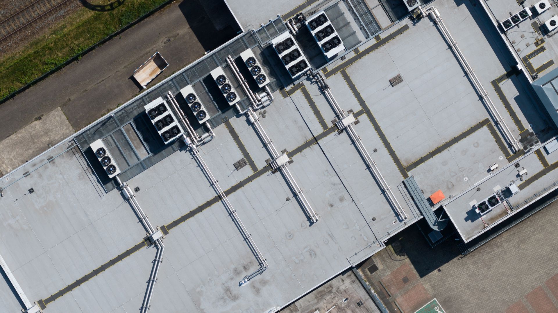 Aerial view of a large white-roofed industrial building with rooftop HVAC units and parking areas.