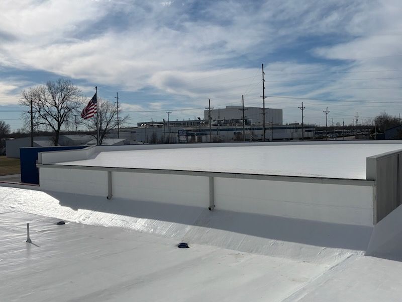 A white flat roof with a raised parapet wall, with an American flag flying in the distance against a blue sky.