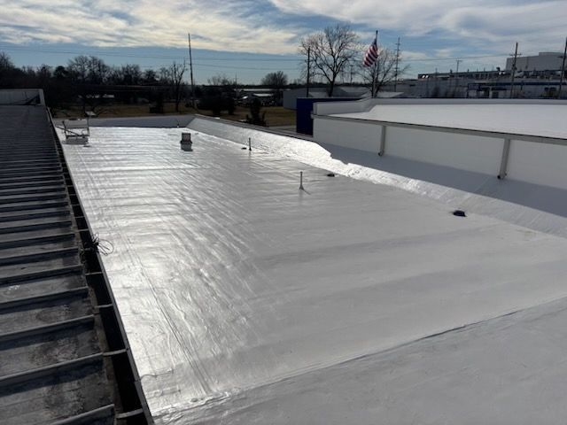 A high-angle view of a newly coated white flat roof under a blue sky, featuring several vent pipes and metal flashing.