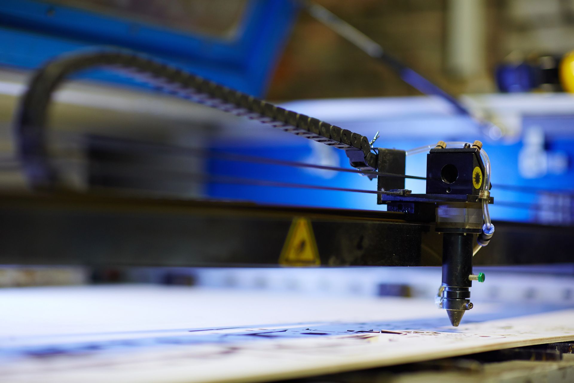 Testa di taglio laser focalizzata su un materiale bianco; braccio meccanico e macchinari sullo sfondo.