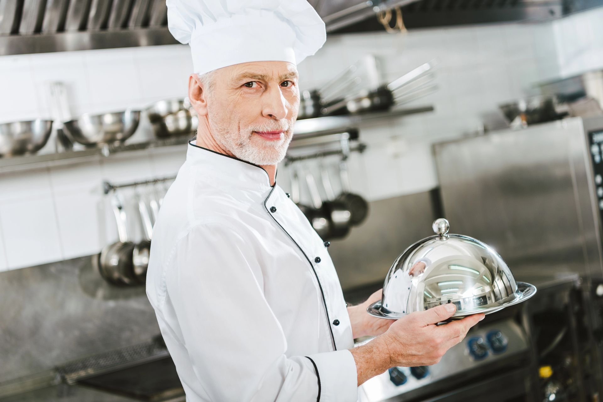 Chef che tiene in mano un piatto da portata d'argento in una cucina commerciale.