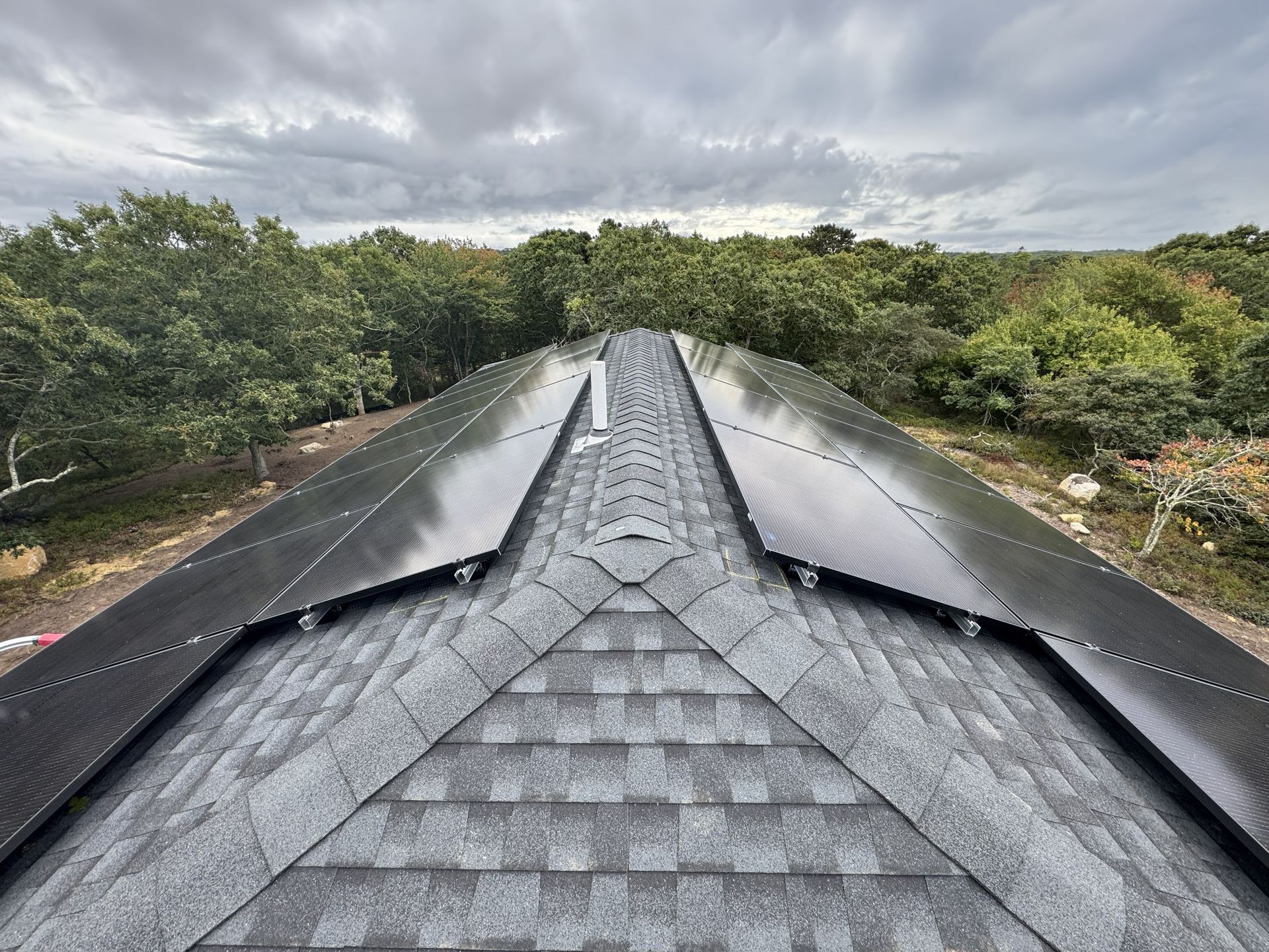 A view from above a roof with shingle tiles, showing black solar panels installed on both sloped sides of the peak.