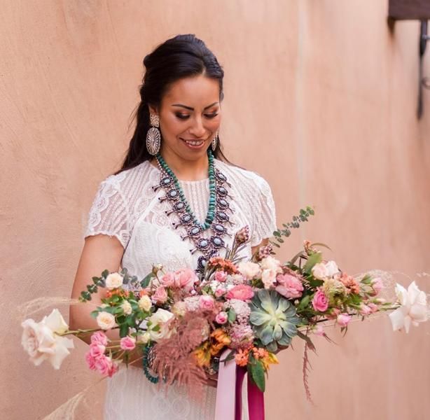 Woman in a white dress holding a large pastel floral bouquet and smiling outdoors