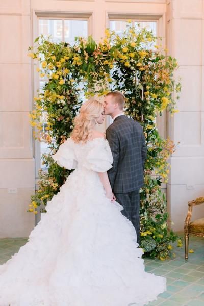 Wedding couple kissing beneath a floral arch at an outdoor ceremony