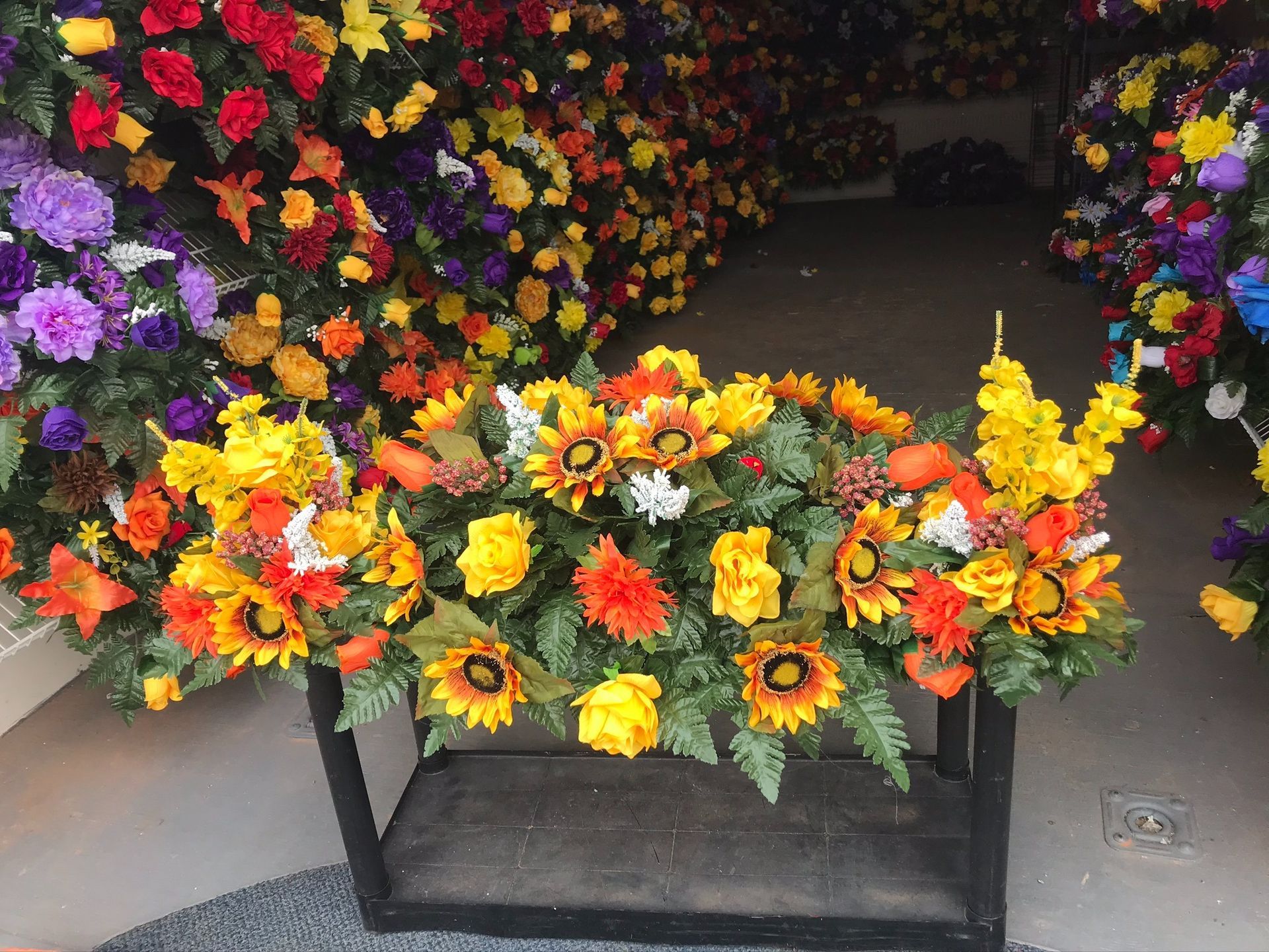 Bright mixed flower arrangements with sunflowers displayed on a black stand at a shop entrance