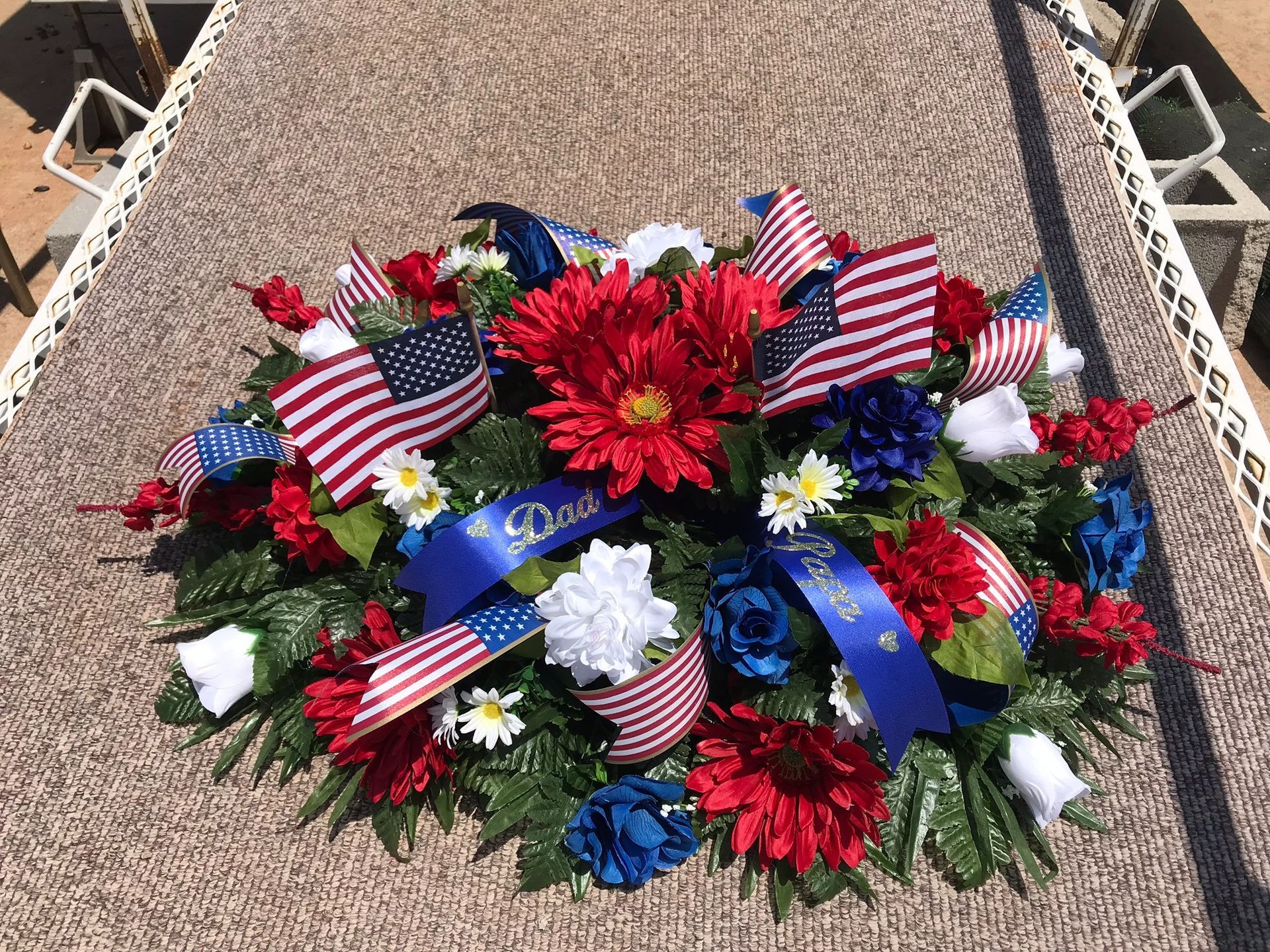 Patriotic memorial wreath with American flags and red, white, and blue flowers on a gravel grave