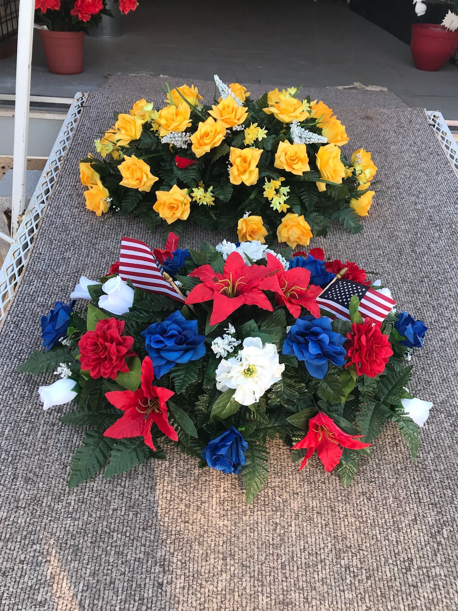 Two colorful flower wreaths, one yellow and one red, displayed on a porch mat