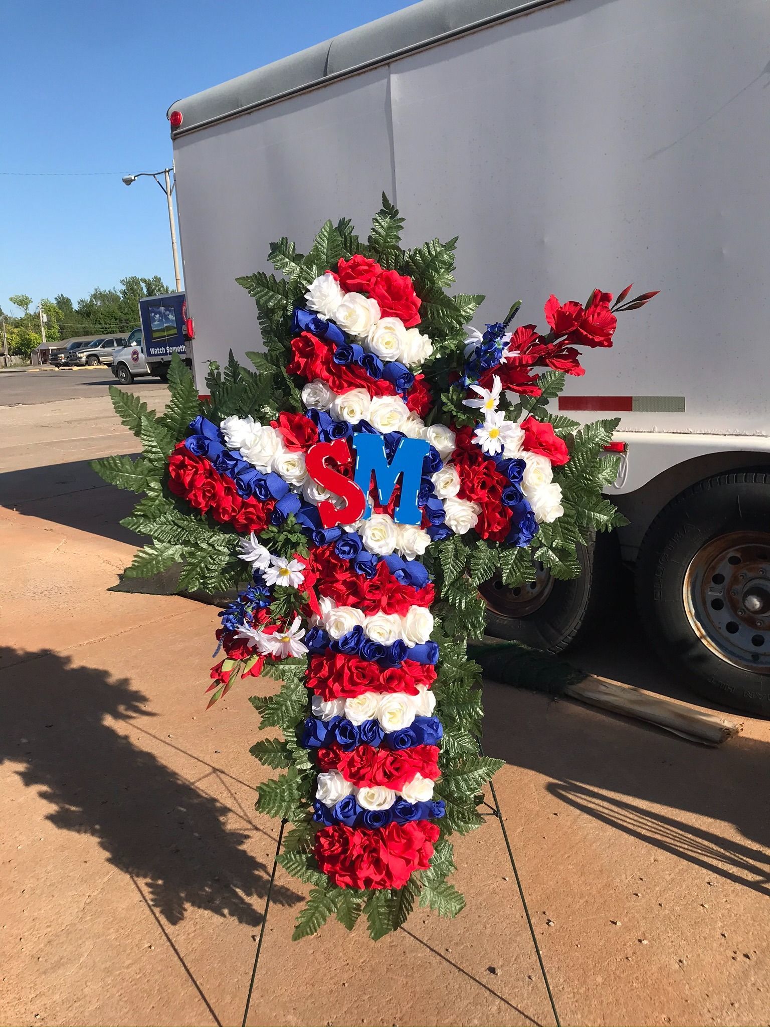 Red, white, and blue floral cross with “SM” on a trailer roadside display