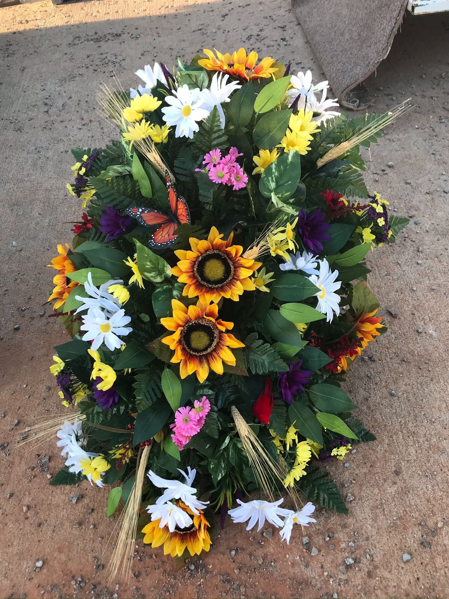 Colorful oval floral wreath with sunflowers, daisies, and greenery on pavement