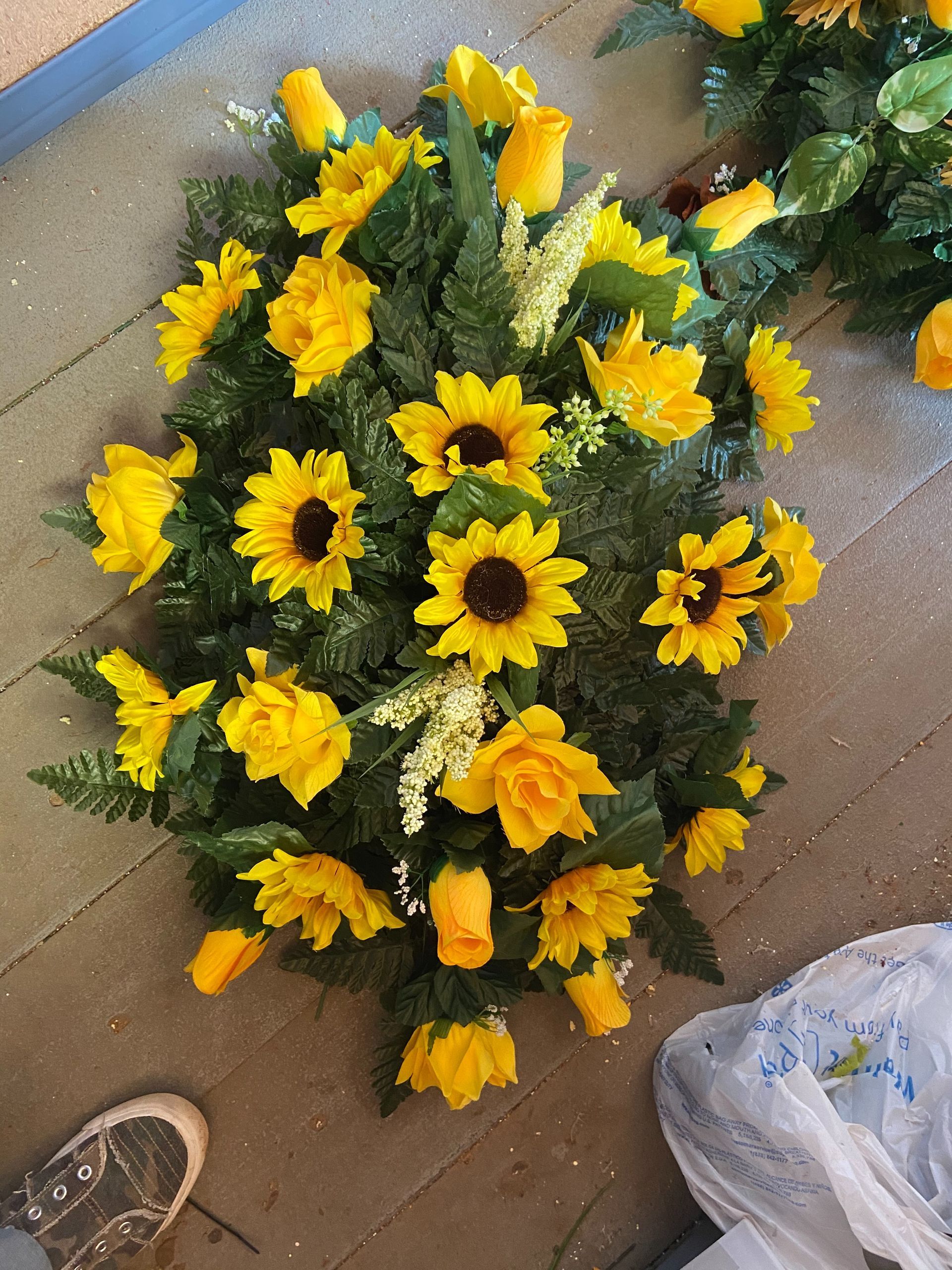 Bouquet of yellow sunflowers and roses on a tiled floor with a sneaker and plastic bag nearby