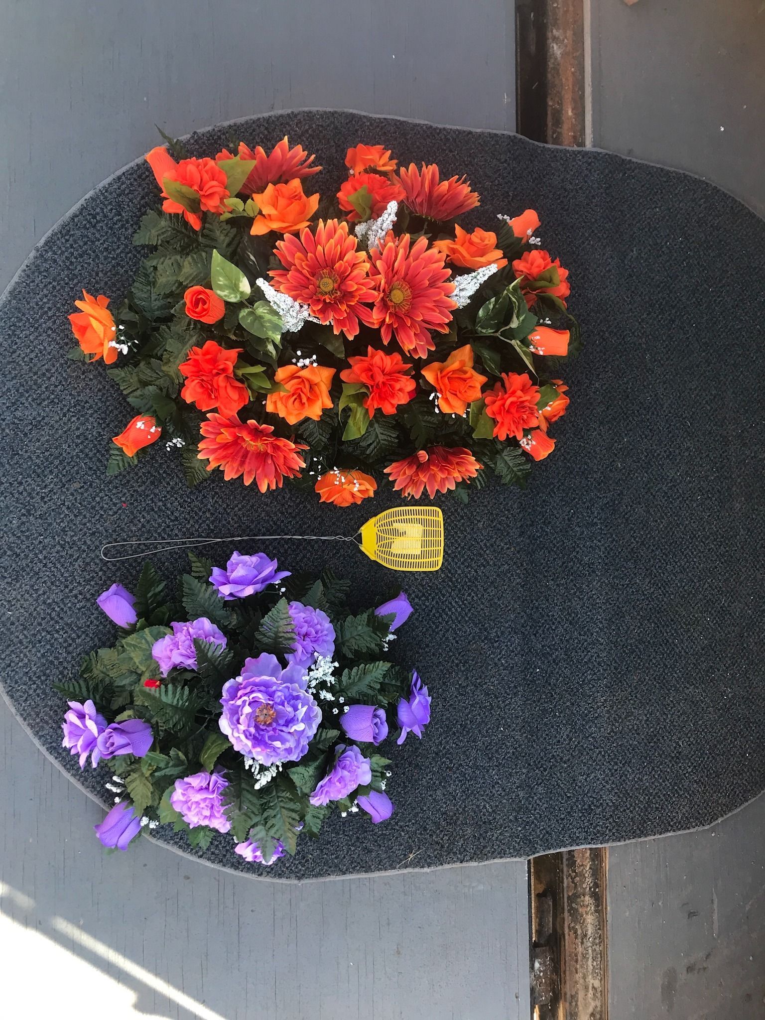 Two flower arrangements, red above purple, on a black stone background with a small yellow plaque