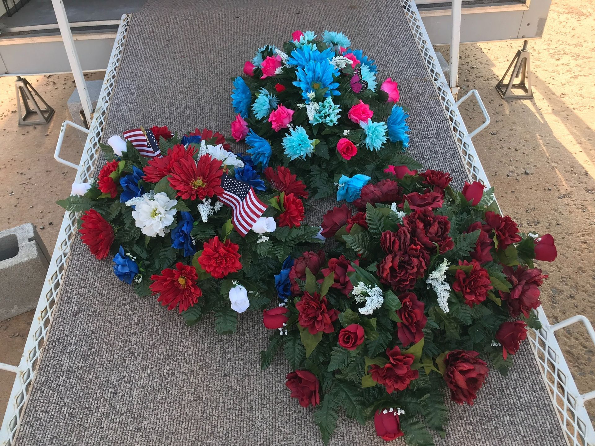 Three colorful floral wreaths on a woven lounge chair outdoors, with red, pink, blue, and white flowers.