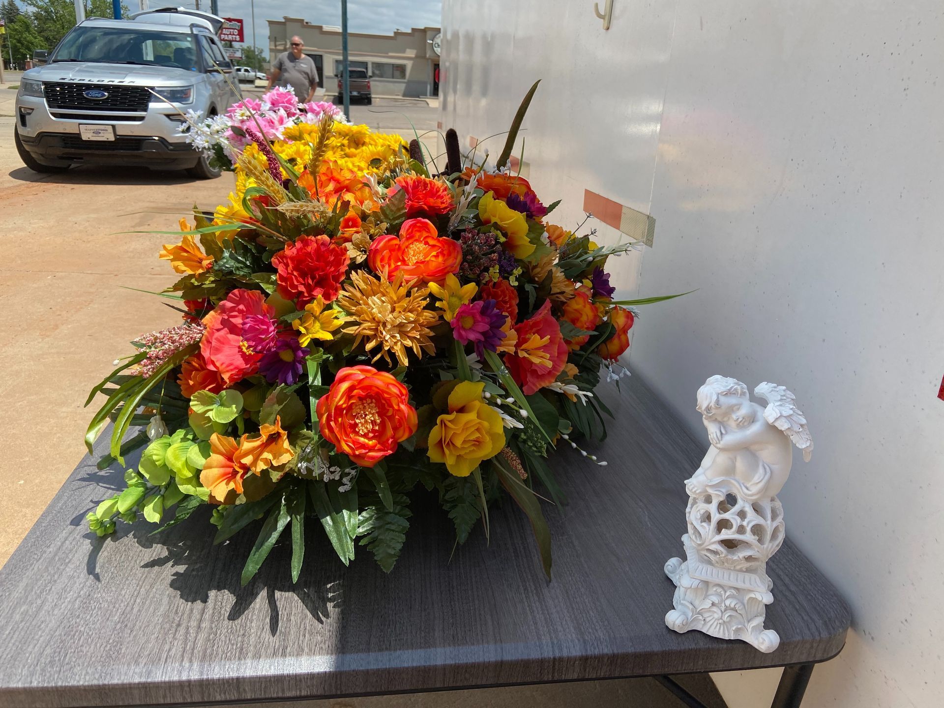 Bright mixed flower bouquet on a table beside a small white angel figurine outdoors