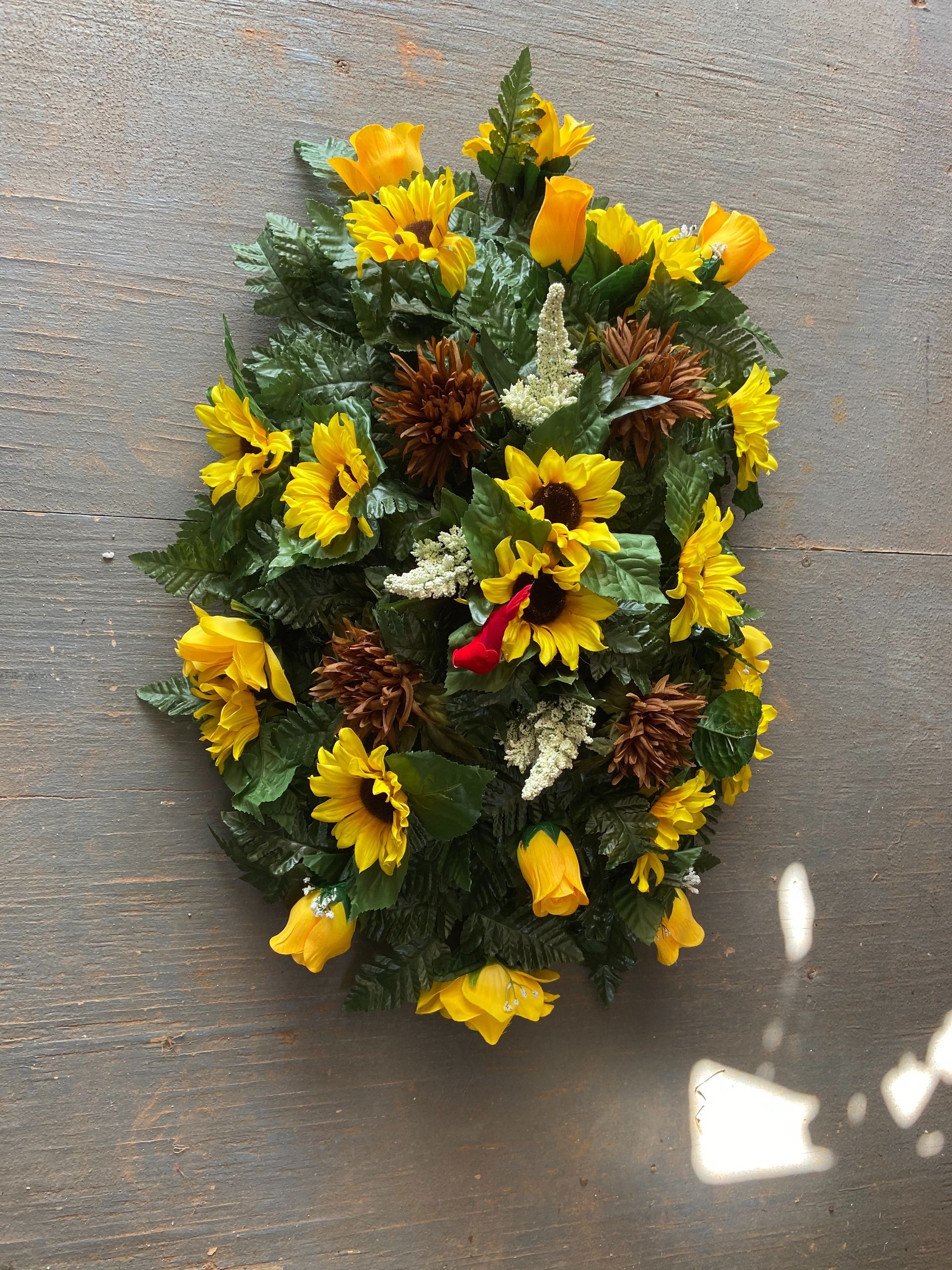 Yellow flower wreath with green foliage and pinecones on a gray wall
